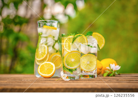 Summer refreshing lemonade drink with ice, and lemon slices on the table in the garden. Fresh healthy cold lemon beverage. copy space 126235556