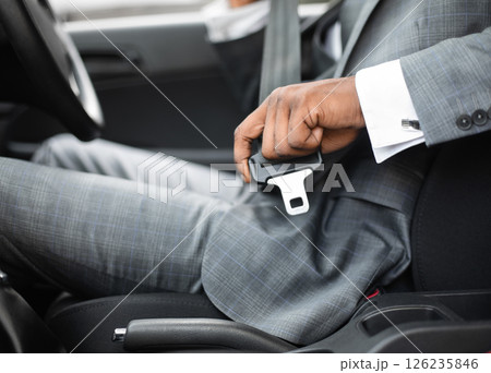 Driving safety concept. Unrecognizable black businessman fasten seat belt in his car, ready to go to office. African american man in stylish suit putting on his seatbelt before driving car, cropped Driving safety concept. Unrecognizable black businessman fasten seat belt in his car, ready to go to office. African american man in stylish suit putting on his seatbelt before driving car, cropped 126235846