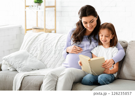Family time. Preschool girl and her expecting mom reading exciting book at home, copy space Family time. Preschool girl and her expecting mom reading exciting book at home, copy space 126235857
