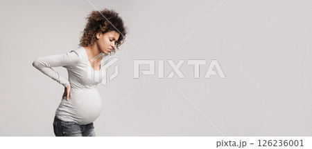 Pregnant woman with contractions, touching her back and suffering from pain, grey background Pregnant woman with contractions, touching her back and suffering from pain, grey background 126236001