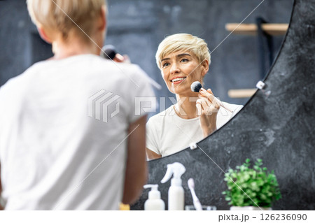 Daily Makeup. Mature Lady Using Cosmetic Brush Applying Face Powder Standing In Bathroom Indoor. Selective Focus, Free Space 126236090