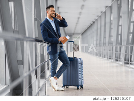 Mobile Call. Smiling Young Middle Eastern Businessman Talking On Cellphone In Airport While Waiting With Suitcase For Flight At Terminal, Happy Arab Man Having Pleasant Phone Conversation Mobile Call. Smiling Young Middle Eastern Businessman Talking On Cellphone In Airport While Waiting With Suitcase For Flight At Terminal, Happy Arab Man Having Pleasant Phone Conversation 126236107