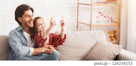 Preschool girl taking selfie with her cheerful father, sitting on sofa at home, copy space Preschool girl taking selfie with her cheerful father, sitting on sofa at home, copy space 126236153