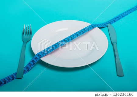Healthy food, fitness for weight loss. An empty plate with a forkknife measuring tape in centimeters on a blue background from above. Diet menu Obesity. Place for an inscription. Advertising. 126236160