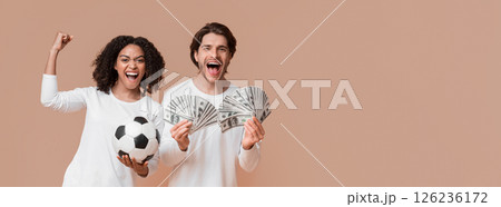 Sports Betting. Euphoric multiracial couple celebrating success with money cash and soccer ball, emotionally reacting to win, yellow background 126236172