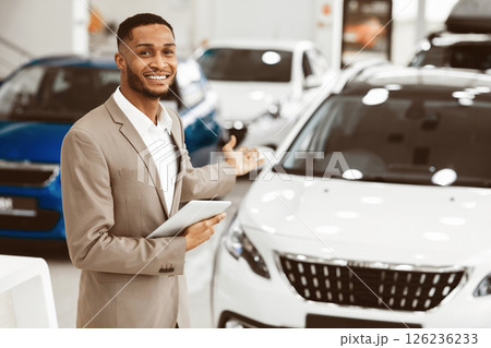 Cheerful Car Dealer Gesturing Showing Brand-New Automobile Standing In Delarship During Luxury Auto Exhibition. Empty Space 126236233