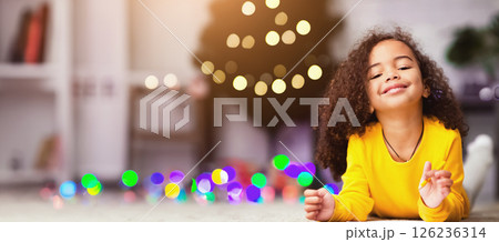 Xmas fun. Cheerful african little girl drawing on floor near decorated Christmas tree at home, free space 126236314