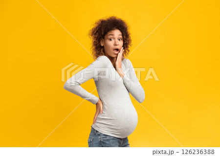 Surprised black pregnant woman closing mouth and looking at camera over pink background 126236388