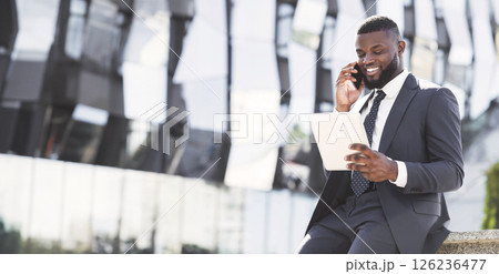 Positive African Entrepreneur Talking On Cellphone Using Digital Tablet During Coffee Break In City Urban Area 126236477