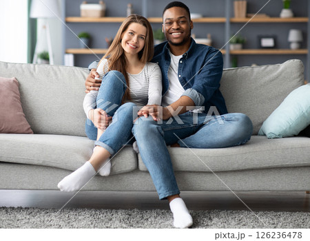 Portrait Of Happy Young Interracial Spouses Posing On Couch At Home, Cheerful Mixed Couple Black Man And White Woman Embracing On Sofa While Relaxing In Cozy Living Room Together, Free Space Portrait Of Happy Young Interracial Spouses Posing On Couch At Home, Cheerful Mixed Couple Black Man And White Woman Embracing On Sofa While Relaxing In Cozy Living Room Together, Free Space 126236478