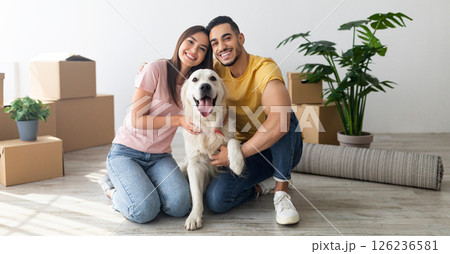 Cheery young international couple with cute golden retriever dog sitting on floor of new home on relocation day. Happy millennial husband and wife with cute pet moving to new house 126236581