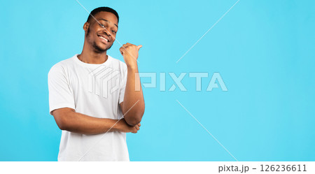 Black Guy Pointing Thumb Aside At Blank Space For Text Standing On Blue Studio Background. Look There Concept. Panorama Black Guy Pointing Thumb Aside At Blank Space For Text Standing On Blue Studio Background. Look There Concept. Panorama 126236611