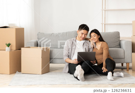 Online Ordering Concept. Asian family using laptop sitting on floor among boxes, empty space Online Ordering Concept. Asian family using laptop sitting on floor among boxes, empty space 126236631