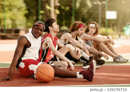 Black basketball player with his diverse team relaxing at outdoor court after championship, free space. Young multiracial sportsmen communicating before game, discussing their tactics Black basketball player with his diverse team relaxing at outdoor court after championship, free space. Young multiracial sportsmen communicating before game, discussing their tactics 126236710