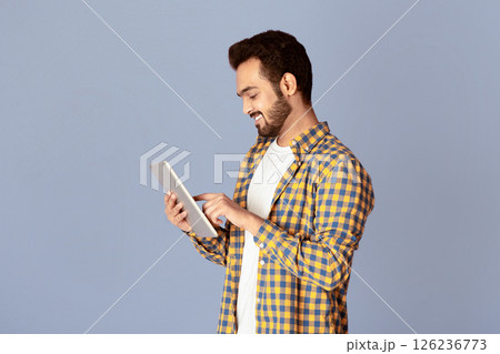 Handsome Indian guy using tablet computer for online work or communication on violet background, panorama 126236773