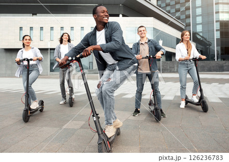 Youth Concept. Portrait of active african american guy driving stand-up scooters in urban area with his friends, full length 126236783