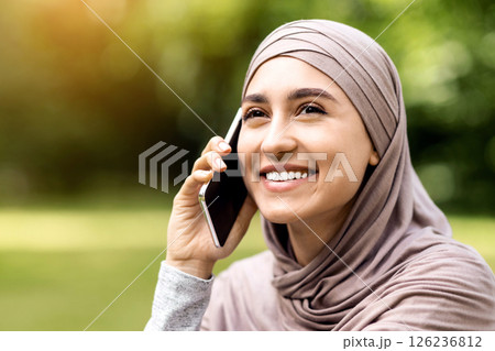 Closeup portrait of happy young muslim woman talking on phone, looking at copy space, park background Closeup portrait of happy young muslim woman talking on phone, looking at copy space, park background 126236812