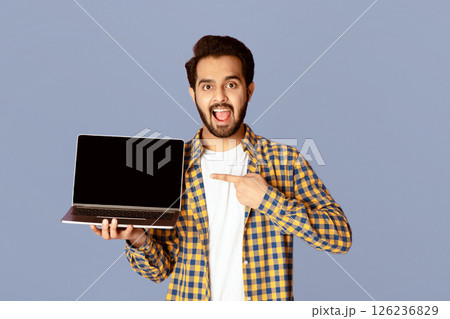 Excited Indian guy pointing at empty laptop screen over violet background, mockup for website design. Panorama Excited Indian guy pointing at empty laptop screen over violet background, mockup for website design. Panorama 126236829