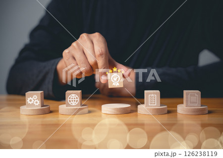 ISO certification concept displayed through smart globe icons with a check mark guarantee icon on a wooden cube. Hand flipping the ISO icons represents quality control management. Business technology ISO certification concept displayed through smart globe icons with a check mark guarantee icon on a wooden cube. Hand flipping the ISO icons represents quality control management. Business technology 126238119