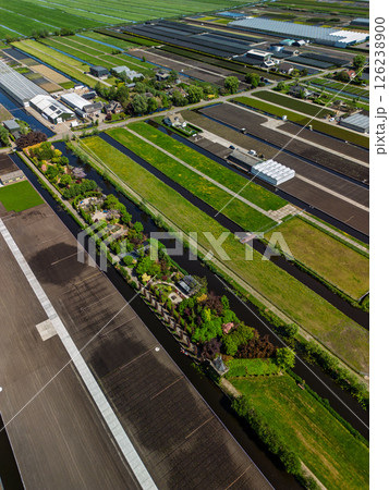 Aerial view of a lush countryside garden surrounded by canals and farmlands, with a cozy house and colorful trees, set in a peaceful rural landscape under a clear blue sky. Aerial view of a lush countryside garden surrounded by canals and farmlands, with a cozy house and colorful trees, set in a peaceful rural landscape under a clear blue sky. 126238900