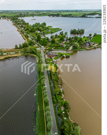 Aerial view of a scenic lakeside village with narrow peninsulas, green fields, and houses surrounded by calm waters under a cloudy sky in the Dutch countryside. 126238905