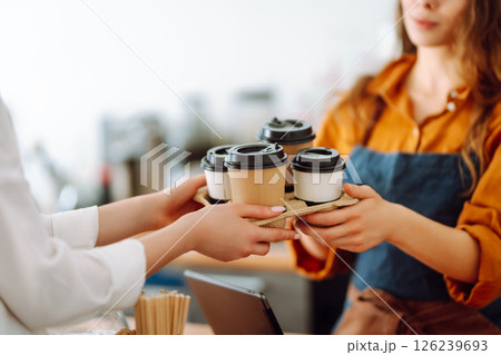 Young woman owner of a coffee shop behind the bar prepares coffee. Concept of orders to go. Young woman owner of a coffee shop behind the bar prepares coffee. Concept of orders to go. 126239693