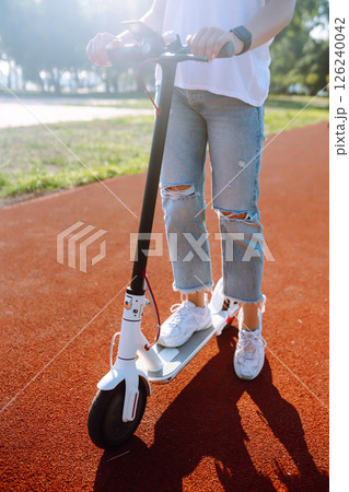 Woman riding electric kick scooter outdoors at sunset, closeup. Ecological transportation concept. 126240042