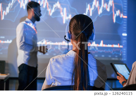 View from behind the woman. Male leader talking to employees, showing the plan on the projector in office View from behind the woman. Male leader talking to employees, showing the plan on the projector in office 126240115