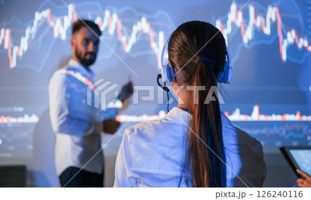 View from behind the woman. Male leader talking to employees, showing the plan on the projector in office View from behind the woman. Male leader talking to employees, showing the plan on the projector in office 126240116