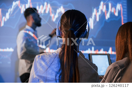View from behind the woman. Male leader talking to employees, showing the plan on the projector in office 126240117