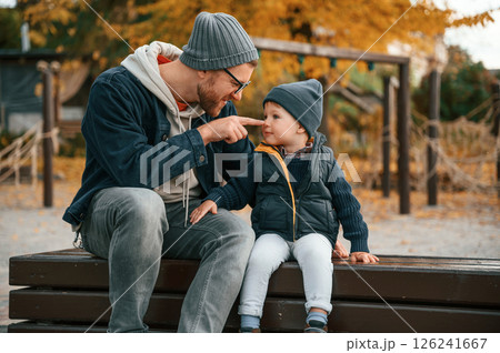 Sitting on the bench and having fun. Father and young son is together outdoors at daytime 126241667