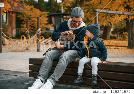 Sitting with cute cat. Father and young son is together outdoors at daytime 126241673