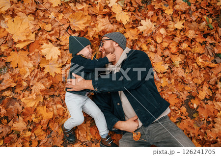 Laying down on the ground that covered with fallen leaves. Father and young son is together outdoors at daytime 126241705