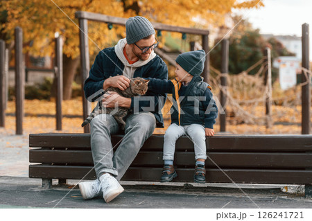 Petting a cat. Father and young son is together outdoors at daytime Petting a cat. Father and young son is together outdoors at daytime 126241721