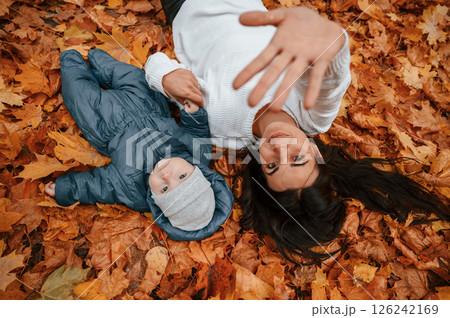 Woman with her little son is laying down on the ground that is covered with autumn fallen leaves Woman with her little son is laying down on the ground that is covered with autumn fallen leaves 126242169