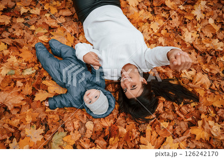 Woman with her little son is laying down on the ground that is covered with autumn fallen leaves Woman with her little son is laying down on the ground that is covered with autumn fallen leaves 126242170