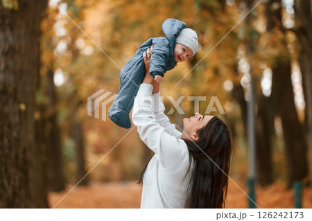 Beautiful mother holding her little son in hands. Standing in the autumn forest Beautiful mother holding her little son in hands. Standing in the autumn forest 126242173