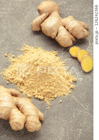 Ginger powder with fresh ginger root on grey concrete background. Top view 126242366