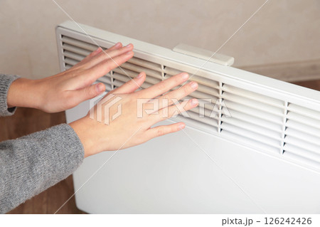 Young woman warming hands near modern electric heater. Space for text 126242426