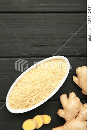 Ginger powder on white plate with fresh ginger root on black wooden background. Top view 126242454