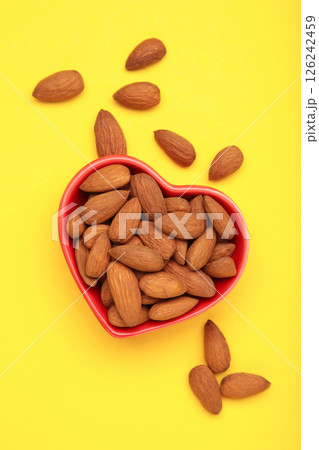 Fresh natural healthy almonds nuts in heart shaped bowl on yellow background. Vertical photo. 126242459