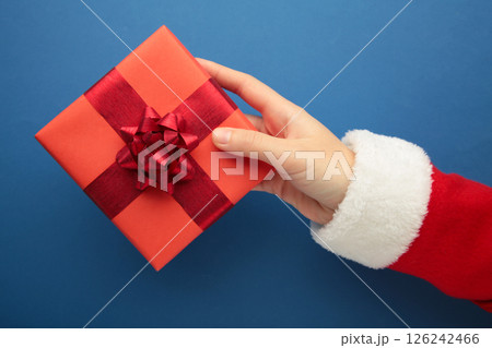 Merry Christmas concept, Top view of Santa claus hands is holding a red gift box on blue background. Merry Christmas concept, Top view of Santa claus hands is holding a red gift box on blue background. 126242466