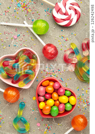 Different types of candies on grey concrete background, copy space. Colorful birthday party background. Vertical photo 126242498