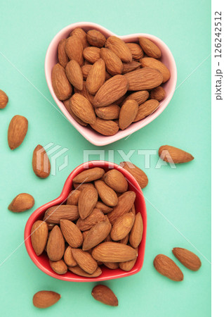 Fresh natural healthy almonds nuts in heart shaped bowl on green background. Vertical photo. Fresh natural healthy almonds nuts in heart shaped bowl on green background. Vertical photo. 126242512
