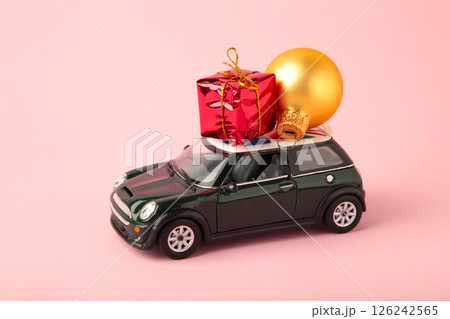 Green toy car with gift on pink background. Concept of celebrating Christmas and New Year. Top view Green toy car with gift on pink background. Concept of celebrating Christmas and New Year. Top view 126242565