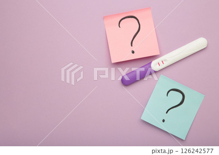 Pregnancy test with two stripes with question marks on purple background. 126242577