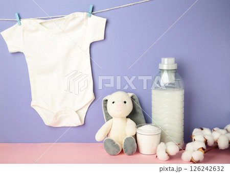 Laundry detergent products with white baby cloth and cotton flower on purple background. Top view 126242632