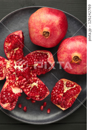 Half-cut pomegranate with seeds in plate on black background. Top view 126242769