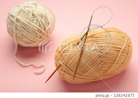 Light knitting yarns and needles on pink background. 126242875