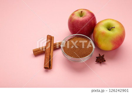 Red apple, cinnamon sticks and cinnamon in bowl on pink background. Red apple, cinnamon sticks and cinnamon in bowl on pink background. 126242901